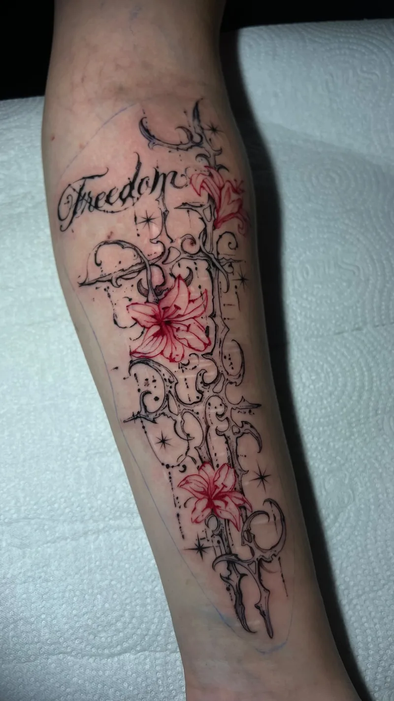 Tatuagem no braço com traços pretos finos e ornamentais, pequenos pontos, estrelas e flores em tinta vermelha