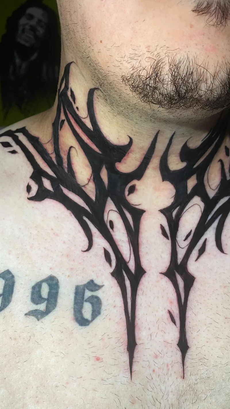 Tatuagem ornamental em tinta preta no pescoço e parte superior do peito, com curvas simétricas e pontas alongadas