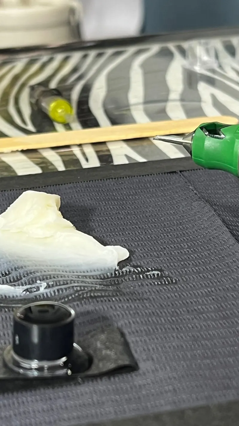 Bancada de tatuagem preparada com máquina, batoque de tinta e papel sobre superfície forrada